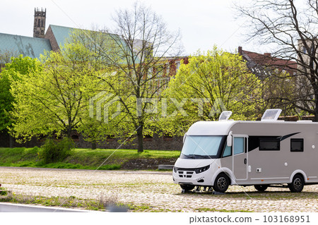 Many white modern campervan recreational motor home vehicles parked in row at camper park site Magdeburg city against Elbe river bridge. Motorhome campground stataion travel destination. RV lifestyle Many white modern campervan recreational motor home vehicles parked in row at camper park site Magdeburg city against Elbe river bridge. Motorhome campground stataion travel destination. RV lifestyle 103168951