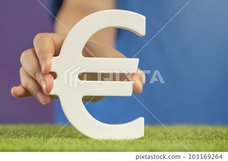 Recession or crisis in Europe. The concept of growth or fall of the economy in Europe. Euro sign in hand on a purple background. Recession or crisis in Europe. The concept of growth or fall of the economy in Europe. Euro sign in hand on a purple background. 103169264