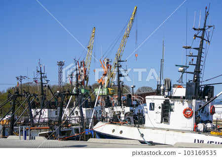 Colorful harbor pier view with small fishing vessels and harbor cranes on blue sky background 103169535