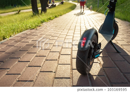 Close-up of an electric scooter on the road in the park at sunset. Eco-friendly transport Close-up of an electric scooter on the road in the park at sunset. Eco-friendly transport 103169595