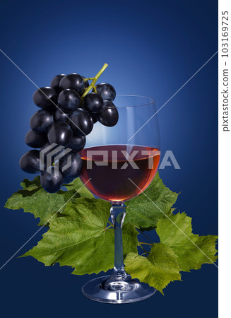 A glass of grape juice with grape leaves on a blue background A glass of grape juice with grape leaves on a blue background 103169725