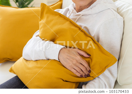 Close-up female hands holding in hands cosy yellow pillow in living room Close-up female hands holding in hands cosy yellow pillow in living room 103170433