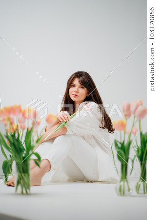 gentle brunette in white sits on the floor with vases of tulips gentle brunette in white sits on the floor with vases of tulips 103170856