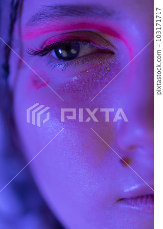Half young female face with shiny stage make-up with sparkles and arrows illuminated with blue and pink neon light. Studio shot of Caucasian ethnicity adult woman looking away. Part of photo series Half young female face with shiny stage make-up with sparkles and arrows illuminated with blue and pink neon light. Studio shot of Caucasian ethnicity adult woman looking away. Part of photo series 103171717
