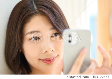 Young woman in plain clothes, living room, smartphone 103172344
