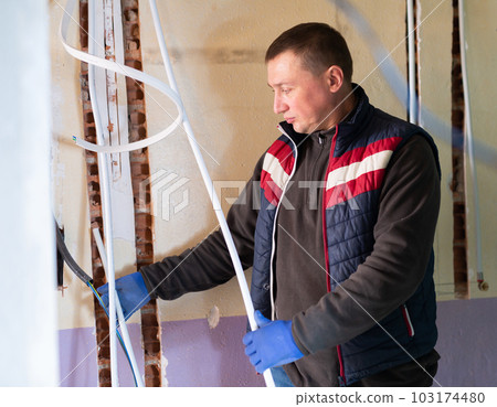 Repair man lying down cable duct in room 103174480