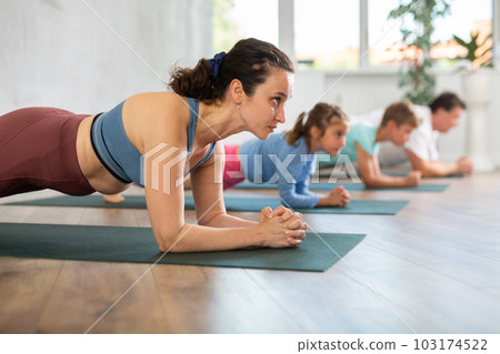 Willing middle-aged woman practicing plank pose of yoga with her family Willing middle-aged woman practicing plank pose of yoga with her family 103174522