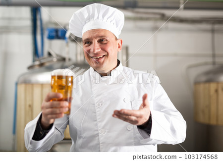 Portrait of brewer who is standing with glass of beer on his workplace in brew-house 103174568