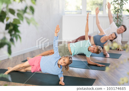Teen girl enjoying yoga class with friendly sporty family in fitness studio, standing in balancing pose Vasisthasana Teen girl enjoying yoga class with friendly sporty family in fitness studio, standing in balancing pose Vasisthasana 103174685