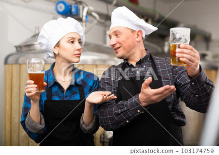 Woman and man brewmasters checking quality of beer and discussing Woman and man brewmasters checking quality of beer and discussing 103174759