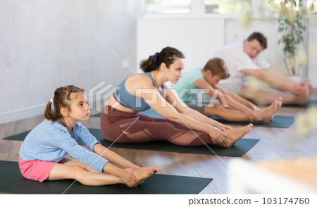 Preteen children with parents doing stretching and doing yoga on mats in gym 103174760