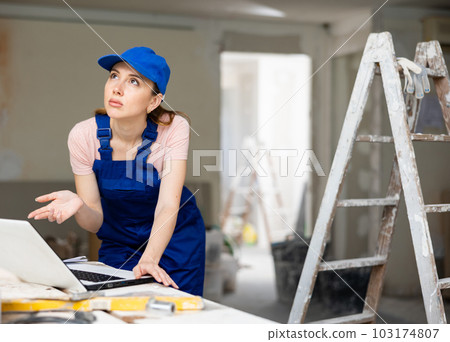 Portrait of a female builder who checks the work done using laptop 103174807