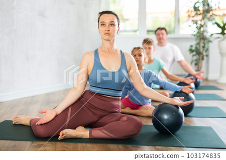 Focused mom, dad, son and daughter doing dove pose with softball, Eka Pada Rajakapotasana Focused mom, dad, son and daughter doing dove pose with softball, Eka Pada Rajakapotasana 103174835