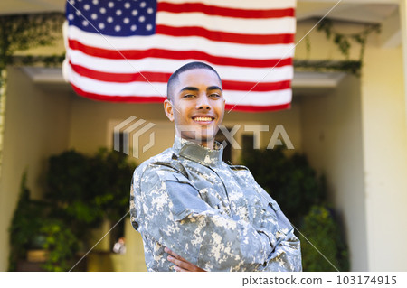 Portrait of happy biracial male american soldier wearing military uniform standing outside the house 103174915