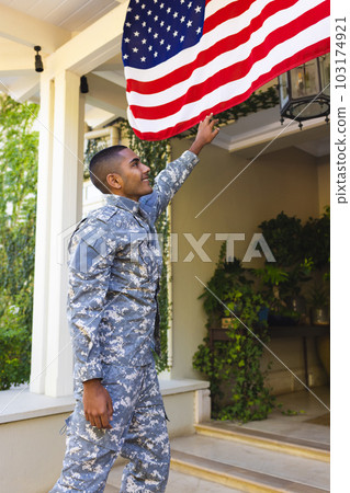 Happy biracial male american soldier wearing military uniform touching flag of usa outside the house Happy biracial male american soldier wearing military uniform touching flag of usa outside the house 103174921