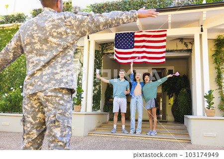 Happy diverse group of friends with usa flags, greeting biracial male american soldier outside house 103174949