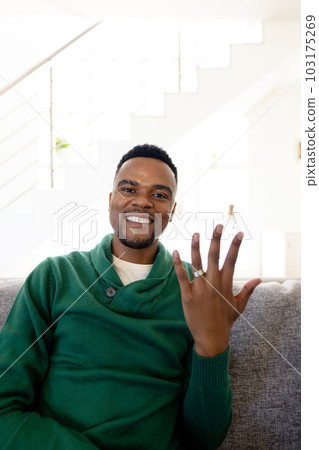 Portrait of african american young man smiling and showing wedding ring while sitting on sofa Portrait of african american young man smiling and showing wedding ring while sitting on sofa 103175269