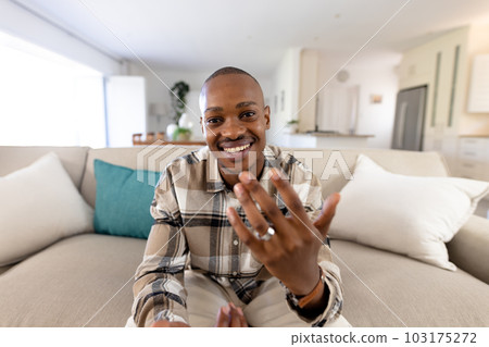Smiling african american man showing wedding ring while sitting on sofa and in living room Smiling african american man showing wedding ring while sitting on sofa and in living room 103175272