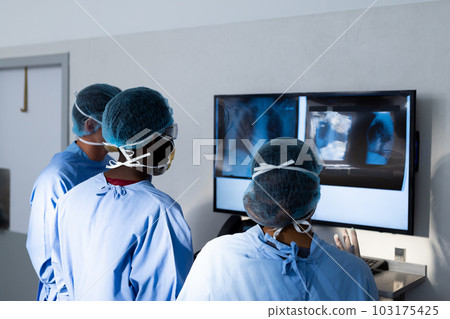 Diverse group of surgeons discussing x rays on screen in operating theatre Diverse group of surgeons discussing x rays on screen in operating theatre 103175425