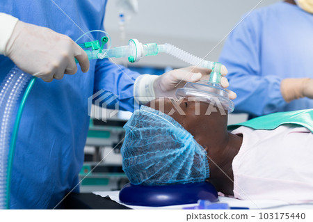 Midsection of surgeon giving african american male patient anesthetic mask in operating theatre Midsection of surgeon giving african american male patient anesthetic mask in operating theatre 103175440