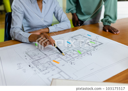 Midsection of african american female architects analyzing blueprint on desk in office, copy space 103175517