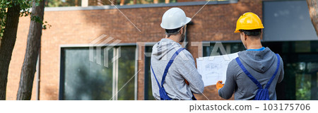 Making the best house. Rear view of two builders standing outdoors with an open blueprint discussing the half completed cottage house 103175706