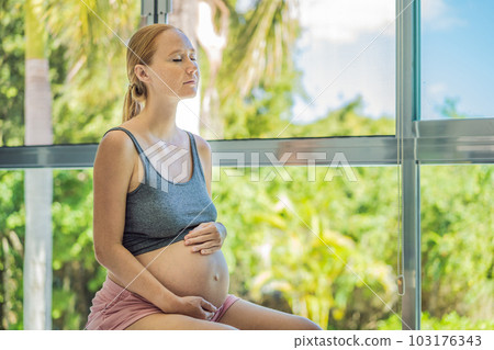 Pregnant woman exercising on fitball at home. Pregnant woman doing relax exercises with a fitness pilates ball. Against the background of the window Pregnant woman exercising on fitball at home. Pregnant woman doing relax exercises with a fitness pilates ball. Against the background of the window 103176343