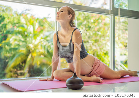 Young pregnant woman doing yoga exercises and meditating at home with an aroma diffuser. Health care, mindfulness, relaxation and wellness concept. Aromatherapy during pregnancy 103176345