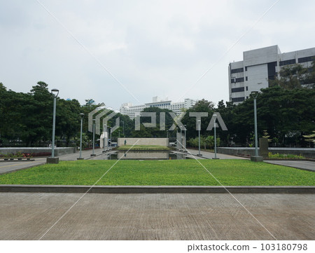 View of people watering the garden yard. This park is surrounded by greenery and several garden lampposts View of people watering the garden yard. This park is surrounded by greenery and several garden lampposts 103180798