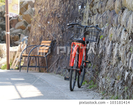 A red bicycle and a bench leaning against a stone wall A red bicycle and a bench leaning against a stone wall 103181414
