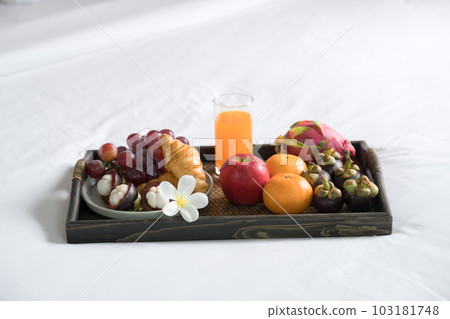 Breakfast, fruit, croissants, orange juice, in a black wooden tray, on a white bedsheet, Healthy food concept 103181748