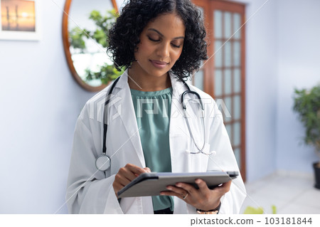 Biracial female doctor wearing sthethoscope, using tablet at doctor's office 103181844