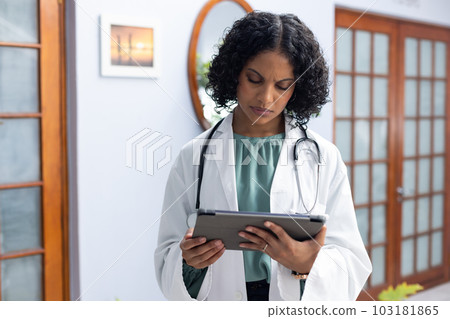 Biracial female doctor wearing sthethoscope, using tablet at doctor's office 103181865