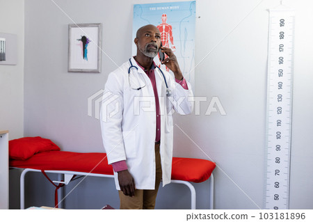 African american male doctor wearing stethoscope talking on smartphone at doctor's office 103181896