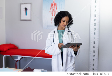 Biracial female doctor wearing sthethoscope, using tablet at doctor's office 103181897