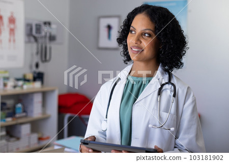 Happy biracial female doctor wearing sthethoscope, using tablet at doctor's office 103181902