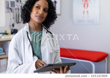 Biracial female doctor wearing sthethoscope, using tablet at doctor's office 103181909