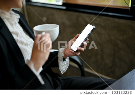A businesswoman is sipping her morning coffee while checking emails on her phone A businesswoman is sipping her morning coffee while checking emails on her phone 103183228