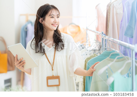 Young female clerk working while operating a tablet in an apparel shop 103183458