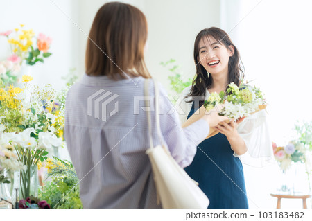 Young female clerk handing a bouquet to a customer in a flower shop 103183482