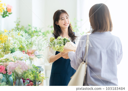 Young female clerk handing a bouquet to a customer in a flower shop Young female clerk handing a bouquet to a customer in a flower shop 103183484