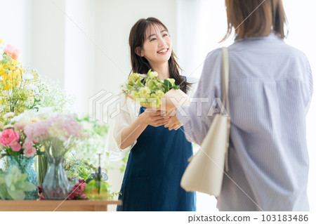 Young female clerk handing a bouquet to a customer in a flower shop Young female clerk handing a bouquet to a customer in a flower shop 103183486