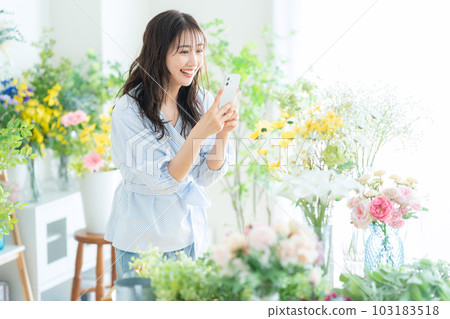 一位年輕的女店員在花店用智能手機拍照 103183518