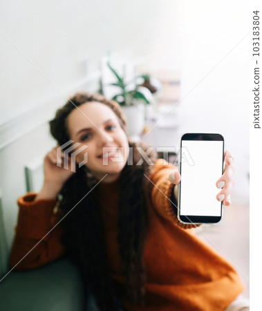 Happy young woman holding mobile phone in hand showing cellphone display, presenting big white blank 103183804