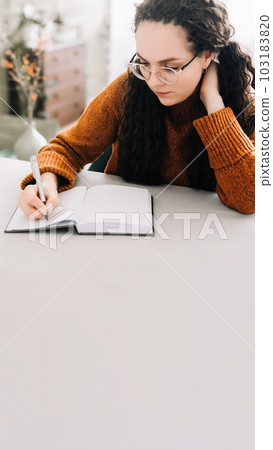 Young woman multitasking: writing in journal and studying for success. Close-up view of woman Young woman multitasking: writing in journal and studying for success. Close-up view of woman 103183820