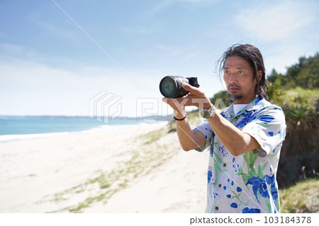 Middle senior man holding a camera at the beach on a sunny day 103184378