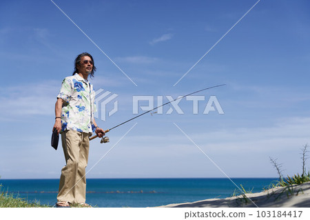 Middle senior man standing with a fishing rod under the blue sky 103184417