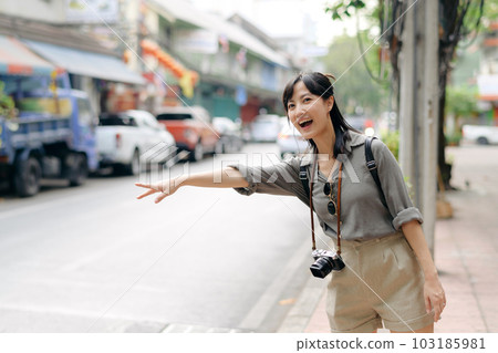 Smiling young Asian woman traveler hitchhiking on a road in the city. Life is a journey concept. 103185981