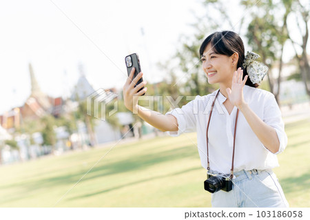 Portrait beautiful young asian woman with smartphone on summer holiday vacation trip with the grand palace in a background at Bangkok, Thailand 103186058