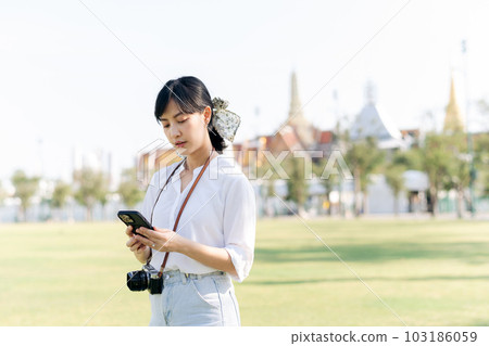 Portrait beautiful young asian woman with smartphone on summer holiday vacation trip with the grand palace in a background at Bangkok, Thailand Portrait beautiful young asian woman with smartphone on summer holiday vacation trip with the grand palace in a background at Bangkok, Thailand 103186059